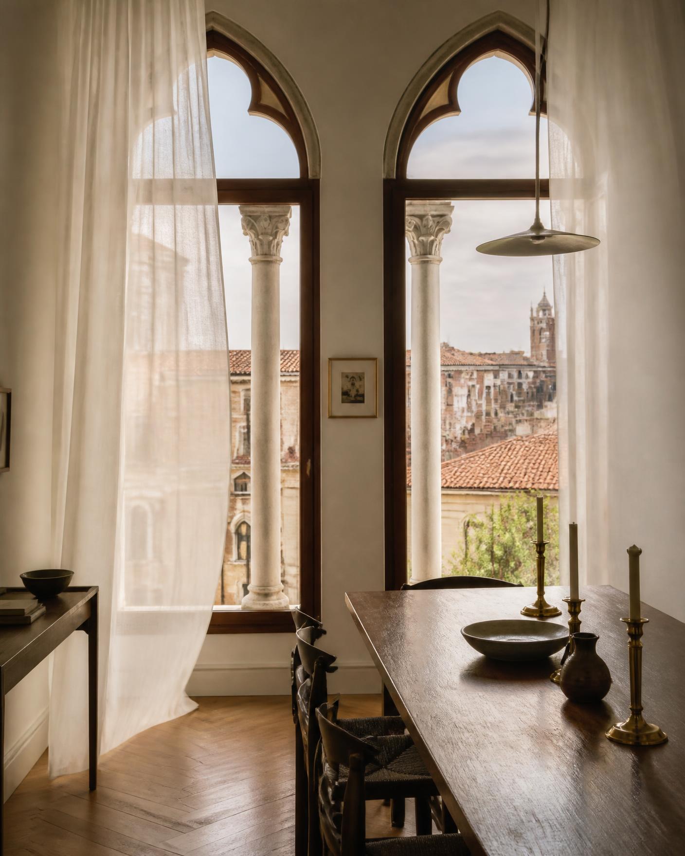 A long walnut table beside tall arched windows overlooking the rooftops of an old city